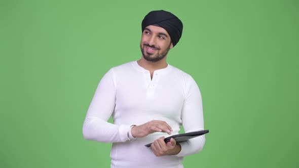 Young Happy Bearded Indian Man Thinking While Using Digital Tablet