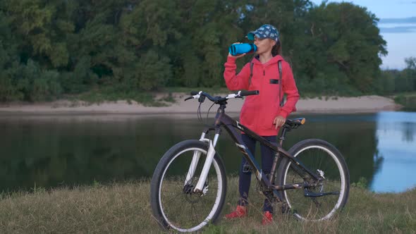 Girl with a bicycle on the nature drinks water. alt