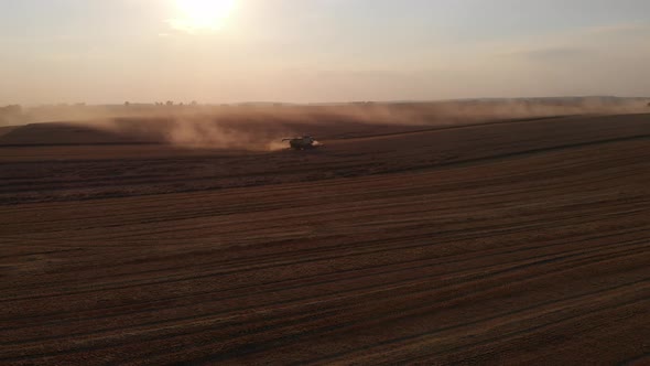 Aerial shot: flying around combine harvesting wheat at sunset