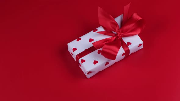 Rotating Gift Box Wrapped in Paper Hearts and Red Bow on Red Background Valentines Day Celebration