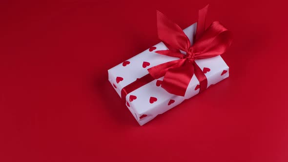 Rotating Gift Box Wrapped in Paper Hearts and Red Bow on Red Background Valentines Day Celebration alt