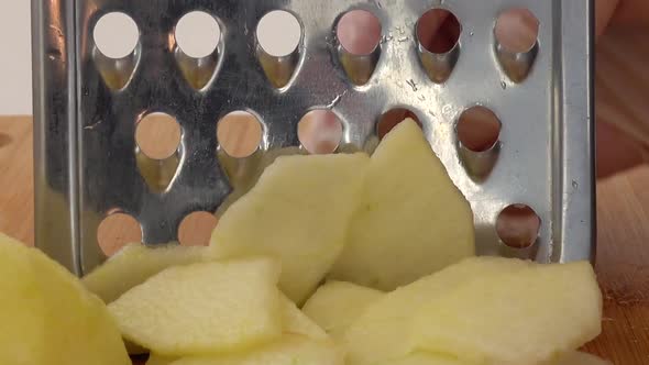 The cook cuts an apple on a grater. alt