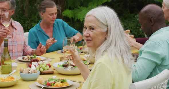 Animation of happy caucasian senior woman eating lunch in garden with diverse friends alt