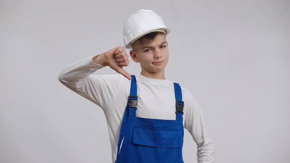 Sad Dissatisfied Caucasian Boy Showing Thumb Down Posing in Builder Uniform at White Background alt