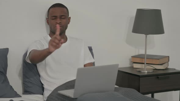 African Man with Laptop Shaking Head As No Sign in Bed alt