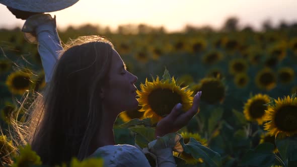 Young Woman with Long Hair and Straw Hat in a Beautiful Field of Sunflowers at Sunset Time alt