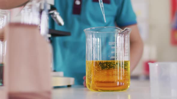 Boy wearing face mask and protective glasses using pipette and beakers in laboratory alt