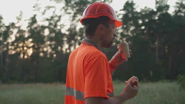 Engineer Having Lunch Near Power Lines and Electricity Pylons in the Field alt
