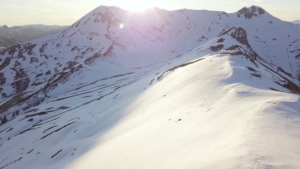 Beautiful Aerial View of Snowy Mountains While Sun is Starting to Set Over Mountain Peak alt