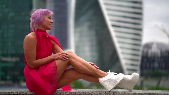 Trendy Dressed Woman in Red Dress and Fashion Boots Is Posing in Urban Landscape alt