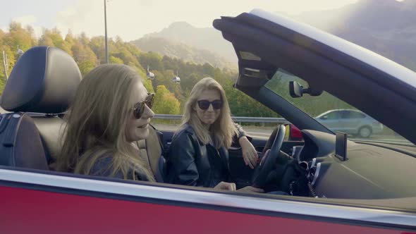 Two Caucasian Girls are Sitting and Talking in a Red Convertible