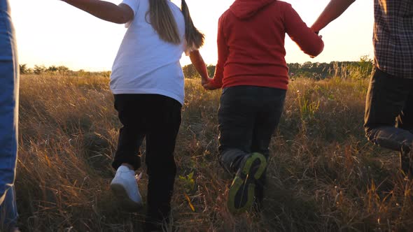 Mom and Dad with Two Kids Holding Hands of Each Other and Running Through Grass Field at Sunset alt