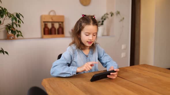 Happy kid girl playing game on mobile phone at home