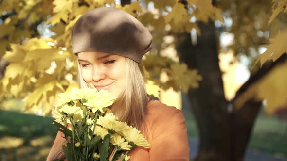 Woman with Bouquet of Chrysanthemums Looks at Camera Smiles and Smells Flowers in Autumn Park
