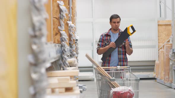Man in a Shirt in a Hardware Store with a Cart Buys a Saw alt