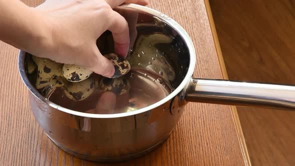Female Hand Puts Quail Eggs Into Empty Stainless Steel Sauce Pot with Mirrored Surface Inside