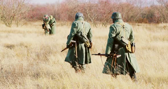 Reenactors Dressed As German Infantry Soldiers In World War II Marching Walking Along Meadow In Cold alt
