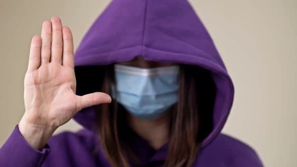 Woman in a Hood and a Medical Mask Demonstrates a Gesture Indicating the Need for Help alt