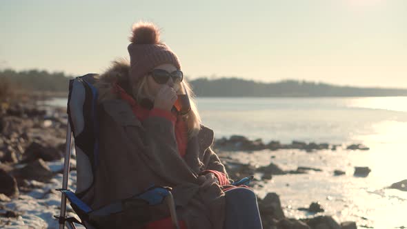 Female Drinking Hot Tea Or Coffee From Mug. Woman Warming Hands Steaming Cup Of Mate Tea. alt