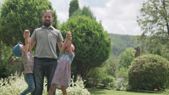 Happy Family Dad with Beard and Siblings Two Preschool Kids Hanging on His Arms alt