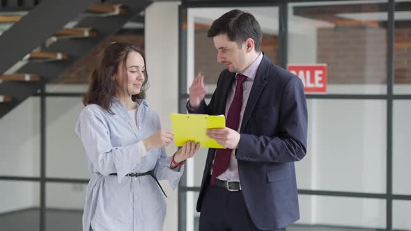 Cheerful Young Beautiful Woman Signing Documents and Receiving Property Key From Man alt