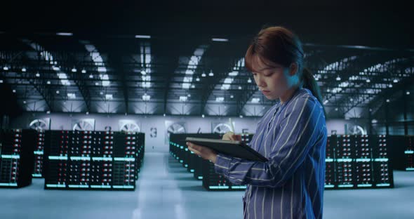 A Young Female Using Tablet While Working in Server Room in Contemporary Data Center