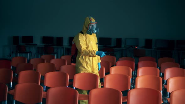 Person in Hazmat Disinfects a Room with Chairs. alt