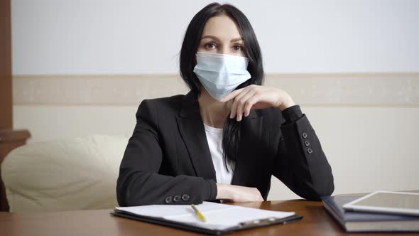 Portrait of Serious Psychologist in Covid19 Face Mask Sitting in Office Looking at Camera alt