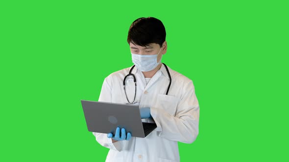 Young Asian Doctor is Working on Laptop Searching and Typing on a Green Screen Chroma Key