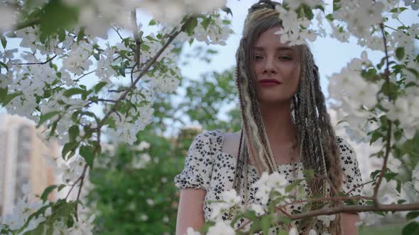 A Cute Girl with Dreadlocks Poses By a Tree with Leaves