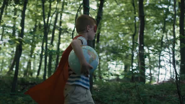 Ginger caucasian boy with superhero costume holding globe and walking in the forest. Shot with RED h alt