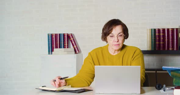An Elderly Caucasian Woman in Glasses Working in Front of a Laptop Monitor She Checks the Report and alt