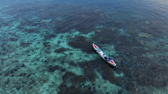 Cinematic aerial view of a fisherman paddling his small boat in the blue ocean.