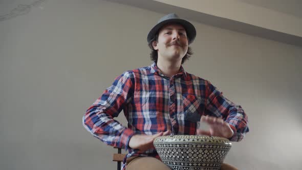 Funny Man with a Mustache and a Hat Playing the Ethnic Drum.