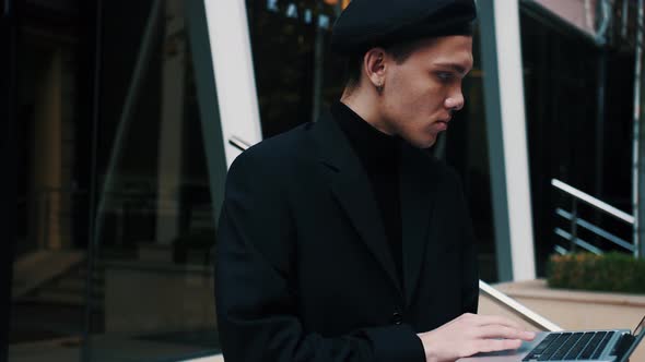 Handsome Young Businessman Sitting on the Stairs Outdoors Working with His Laptop.  alt