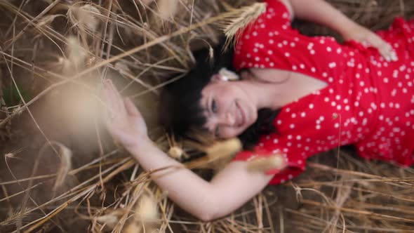 Beautiful Stylish Woman with Dark Hair in a Red Dress in a Field with Hay