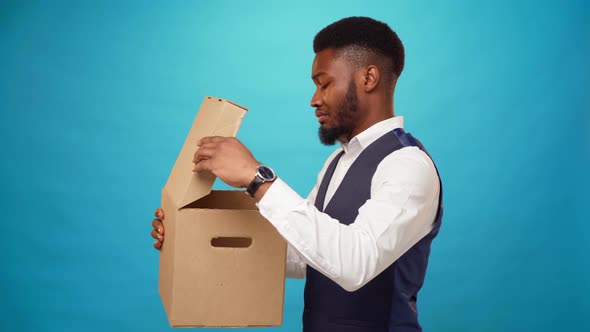 Young African Man Opens Carton Box Dislike What's in It Against Blue Background alt
