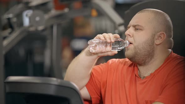 Chubby Overweight Man Is Holding Bottle of Water and Drinking for Little Break Between Heavy