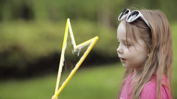 Confident Playful Little Cute Girl Blowing Huge Air Soap Bubble Blower Medium Close-up