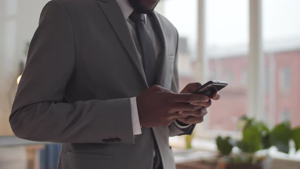 Midsection Shot of Black Businessman Standing in Office and Using Smartphone alt