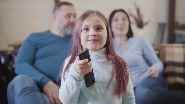 Excited Caucasian Charming Girl Using Remote Control and Making Surprised Facial Expression. Blurred alt