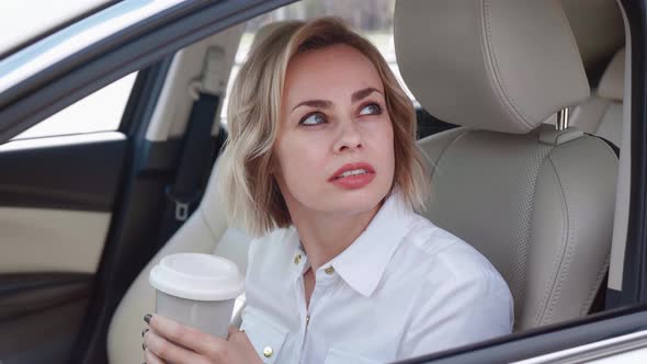 Smiling Business Woman in White Shirt Sitting in the Car and Drinking Coffee alt