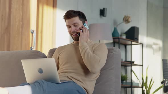 Young man talking on the phone at home office. Working man with laptop alt