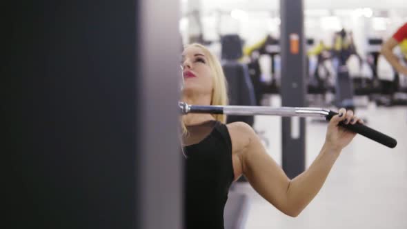 Attractive Young Blond Caucasian Woman with Sporty Body Training Hard on a Lat Pulldown Mashine at alt