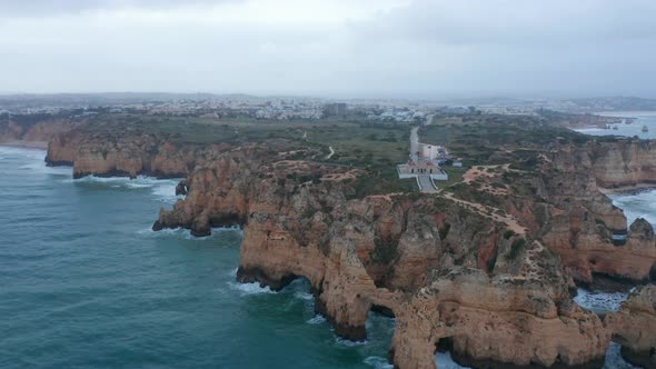 Amazing Aerial Drone View of Lagos Portugal Rocky Coastline with Lighthouse Cloudy Grey Day Circle alt