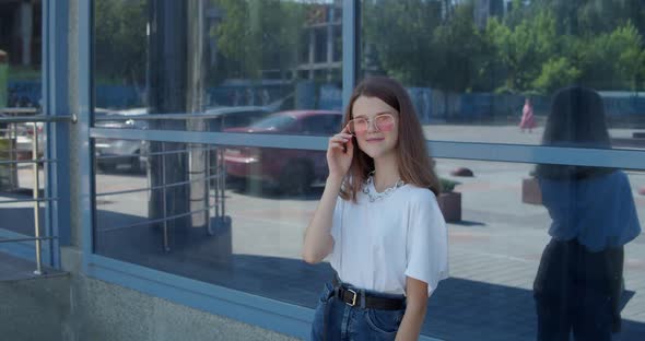 Stylish Teen Poses at Camera When Corrects Sunglasses on Glass Background alt