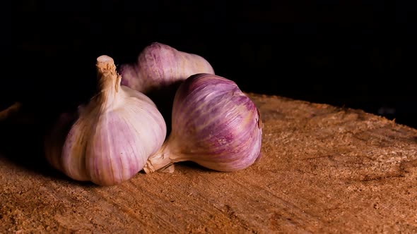 A head of garlic rotates on a wooden table in the dark.
