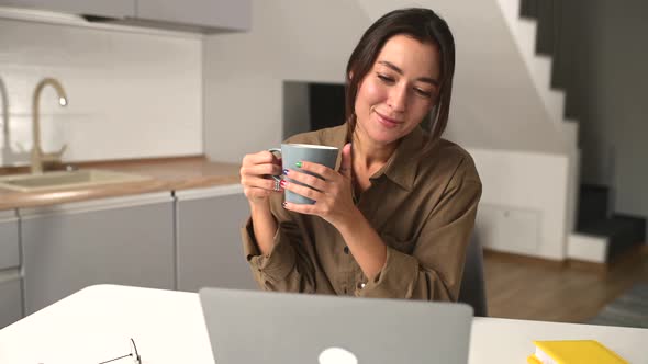 Relaxed Asian Multiracial Female Freelancer Relaxing Sitting with Cup of Coffee in Front of Laptop