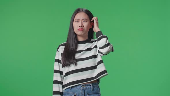 A Puzzled Asian Woman Is Standing In Front Of Green Screen Background alt