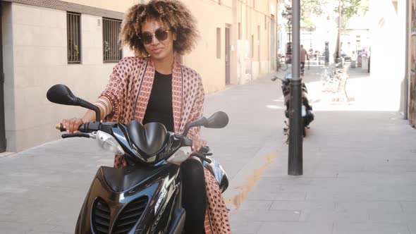 Trendy Ethnic Woman Sitting on Scooter on Street alt